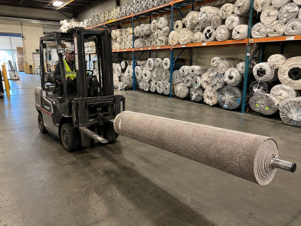 Warehouse worker moving a large carpet roll with a forklift